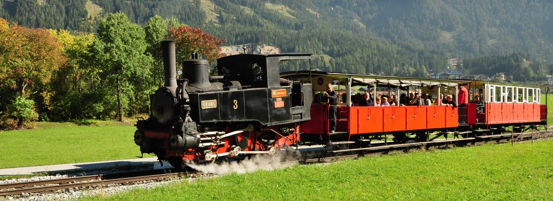 Die schwarze Achenseebahn auf den Gleisen vor Bergkulisse.