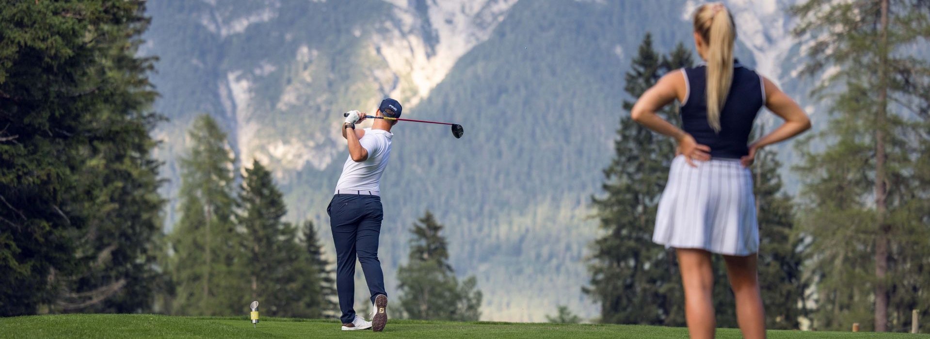 Eine Frau beobachtet einen Mann beim Golf spielen.