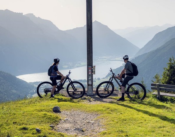 Zwei Radfahrer stehen an einem Gipfelkreuz.