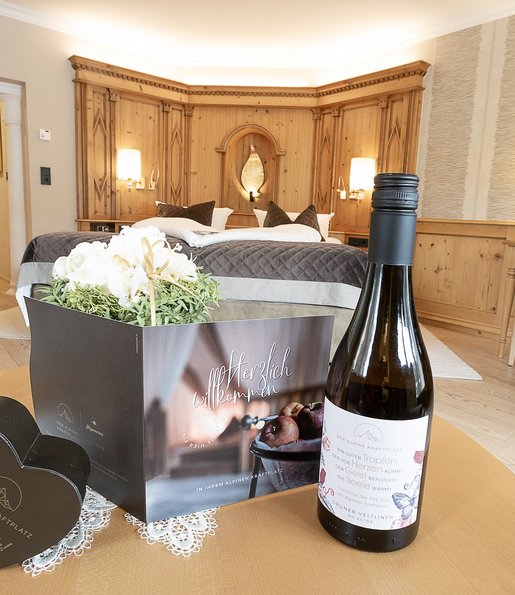 Auf einem Tisch im Hotelzimmer steht eine Willkommenskarte und eine Flasche Weißwein.
