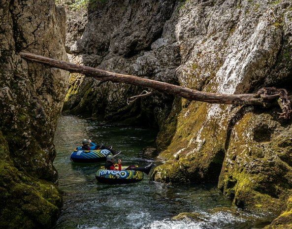 Mehrere Personen treiben auf aufblasbaren Reifen einen Fluss hinunter.