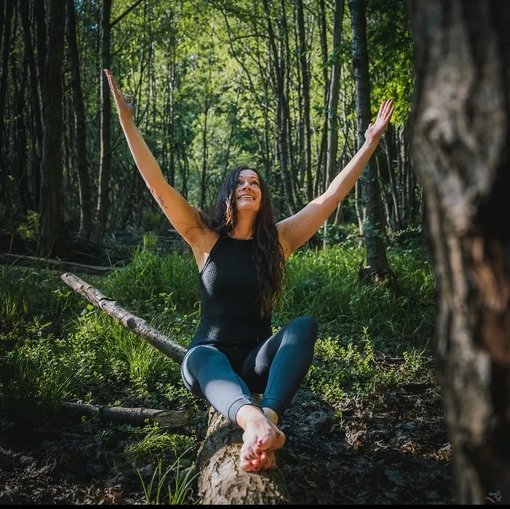 Eine lachende Frau sitzt im Wald auf einem Baumstamm.