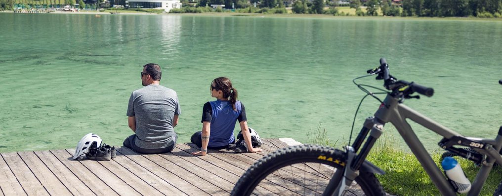 Zwei Radfahrer machen gemeinsam eine Pause am Ufer des Achensees.