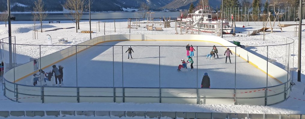 Kinder fahren über einen zugefrorenen Eislaufplatz.