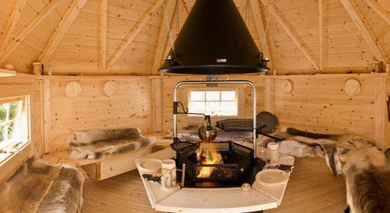 Innenansicht einer finnischen Grillhütte mit rustikaler Einrichtung und Feuerstelle.