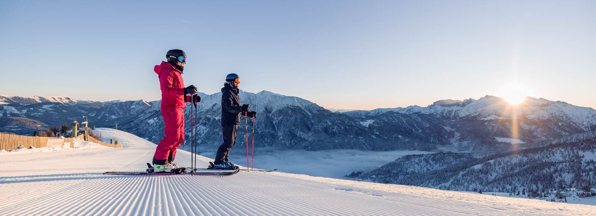 Zwei Skifahrer beobachten den Sonnenaufgang auf der Piste.