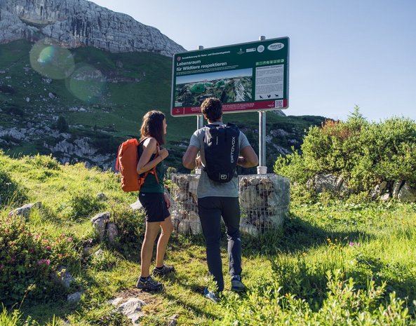 Ein Mann und eine Frau stehen vor einem Lehrpfad im Rofangebirge.