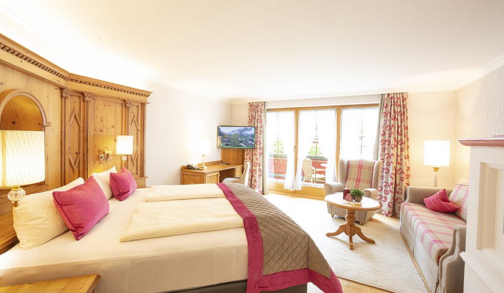 Blick in ein Hotelzimmer mit Doppelbett, Sofa, Fernseher und Balkon.