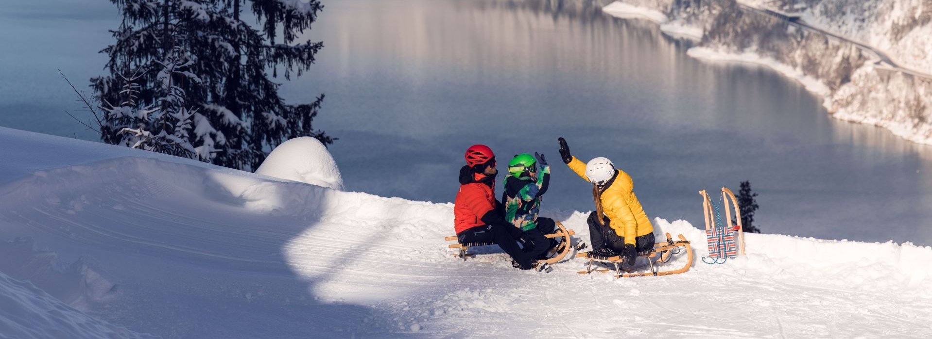 Eine Familie sitzt mit Rodeln im Schnee.