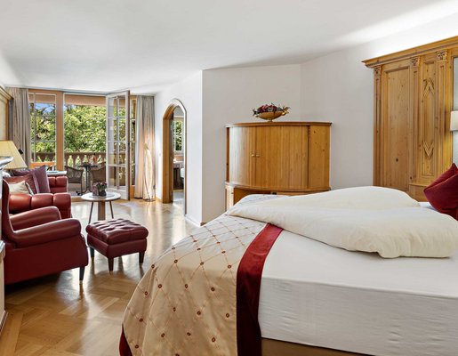 Großes Doppelbett, ein Sofa und ein Sessel in einem Hotelzimmer mit Balkon.